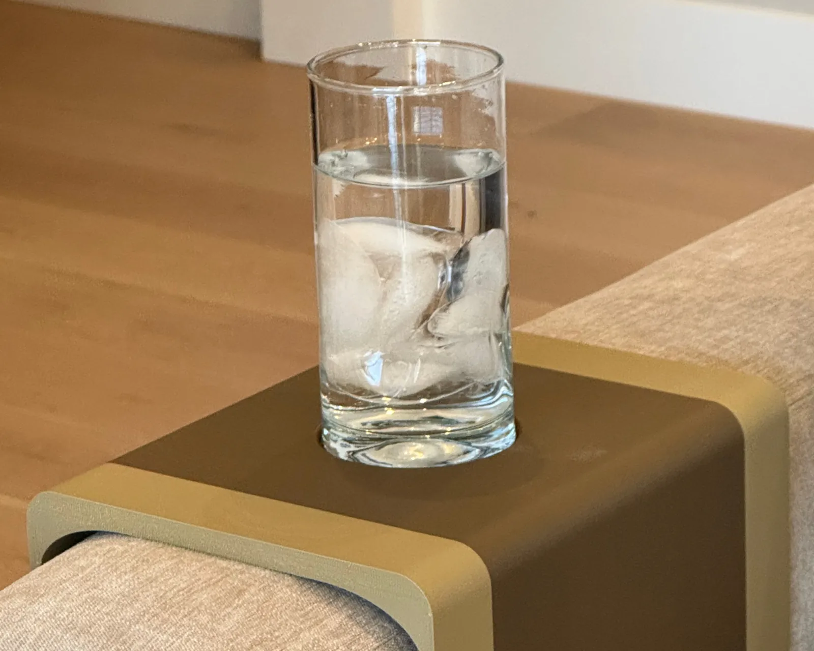 A glass of ice water on the two-tone Sectional Arm Tray, over a light gray fabric sofa arm